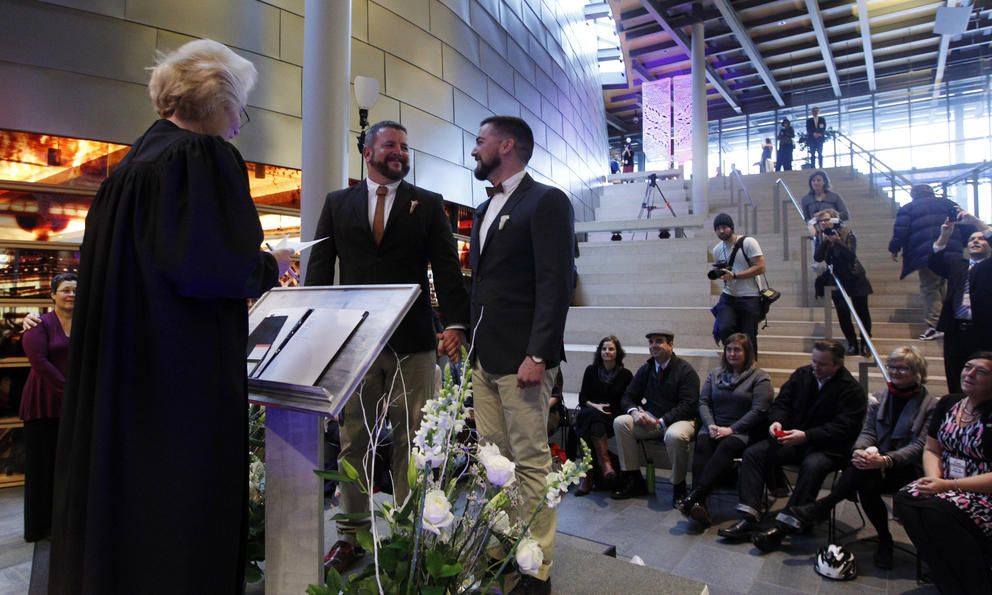 Two men stand together as a judge marries them inside Seattle City Hall