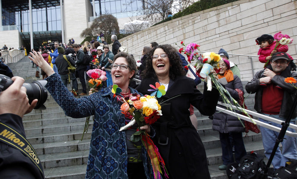 two women laugh and hold flowers surrounded by people on the steps of Seattle City Hall