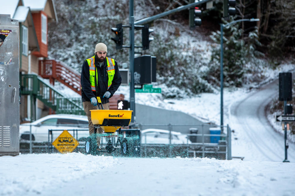 A city worker spreads deicer on a snowy sidewalk