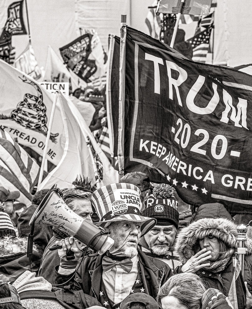 Person stands amid Trump and "Don't Tread on Me" flags in a black and white photo