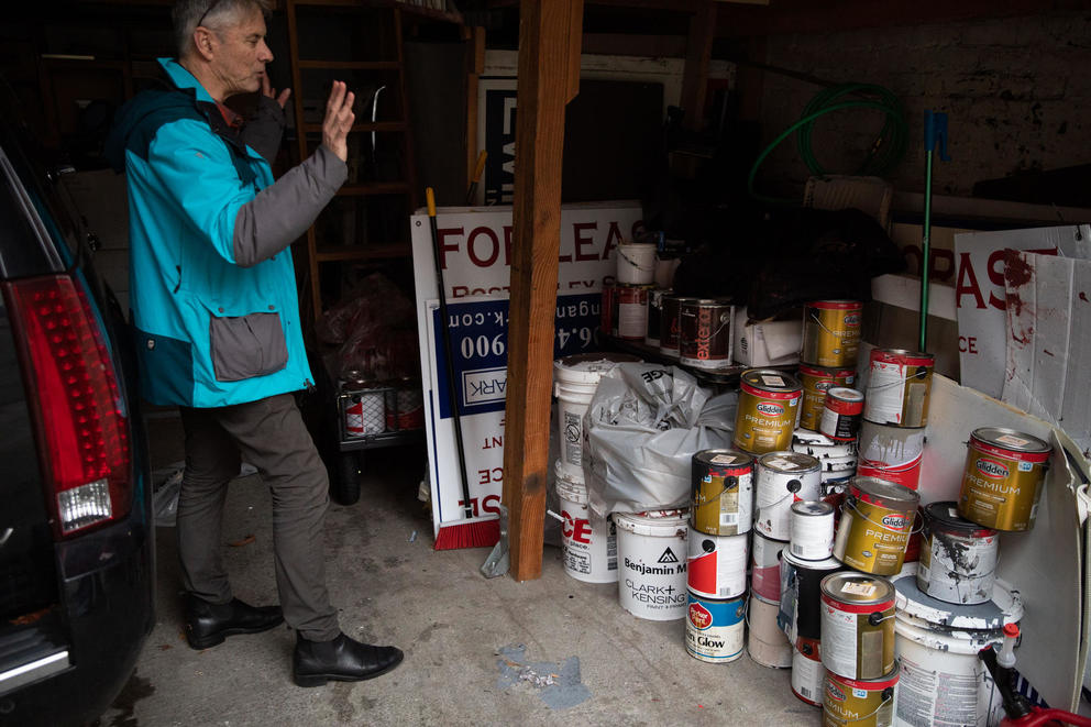 Man stands in garage next to dozens of buckets of paint