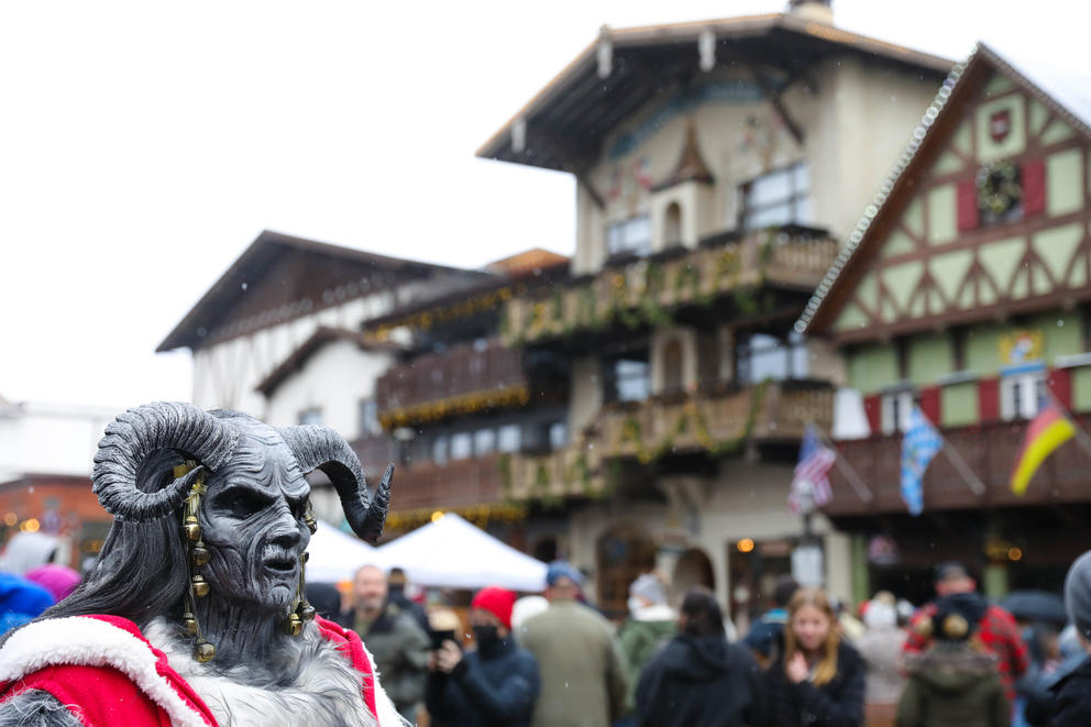 A person in costume as a grey Krampus with horns is in the foreground as the Bavarian-style buildings of Leavenworth are behind her