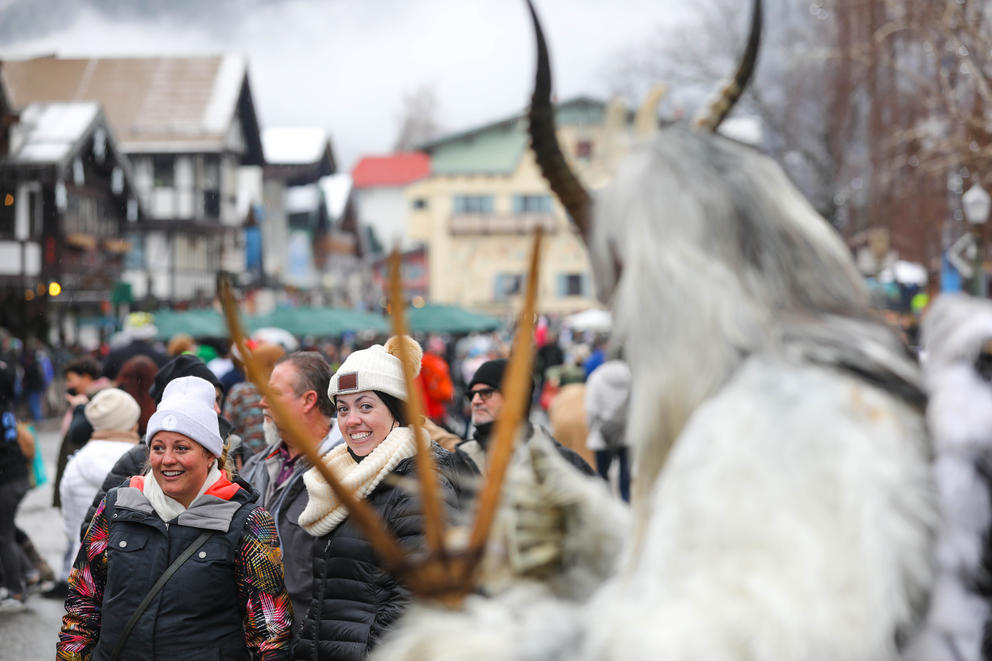 Pedestrians stare at a Krampus, out of focus in the foreground. 