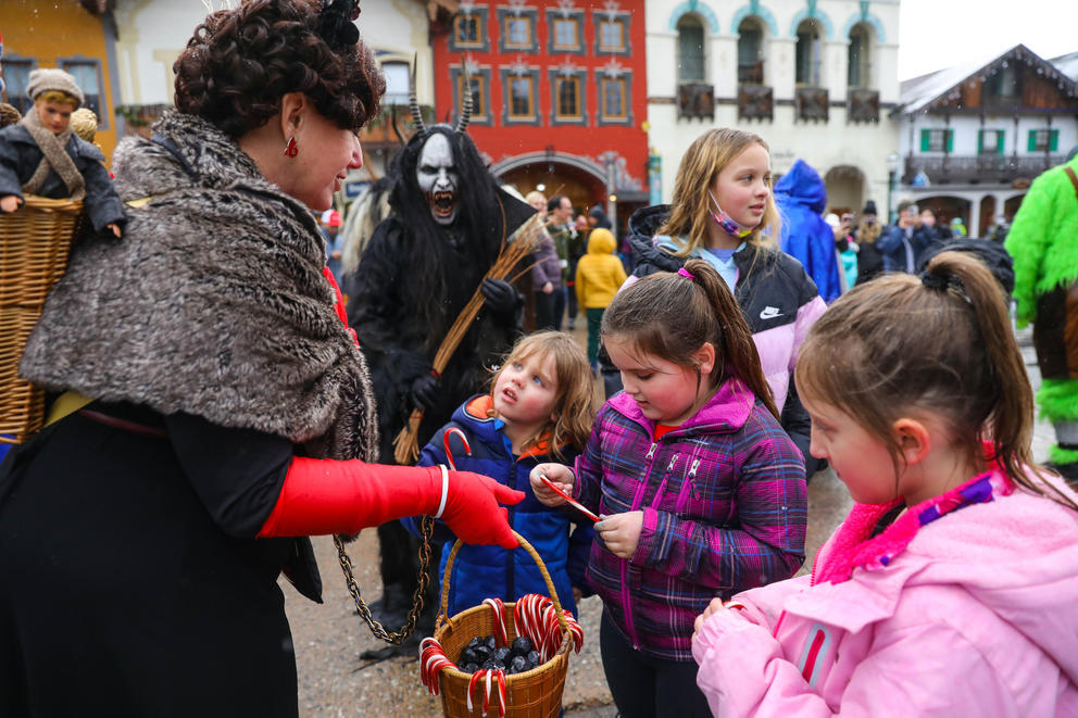 A woman dressed as Lady Krampus hands out candy to children from a basket