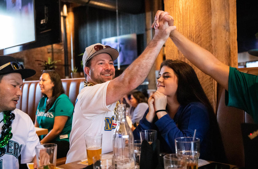 A man high fives someone out of frame over a woman as they sit in a bar