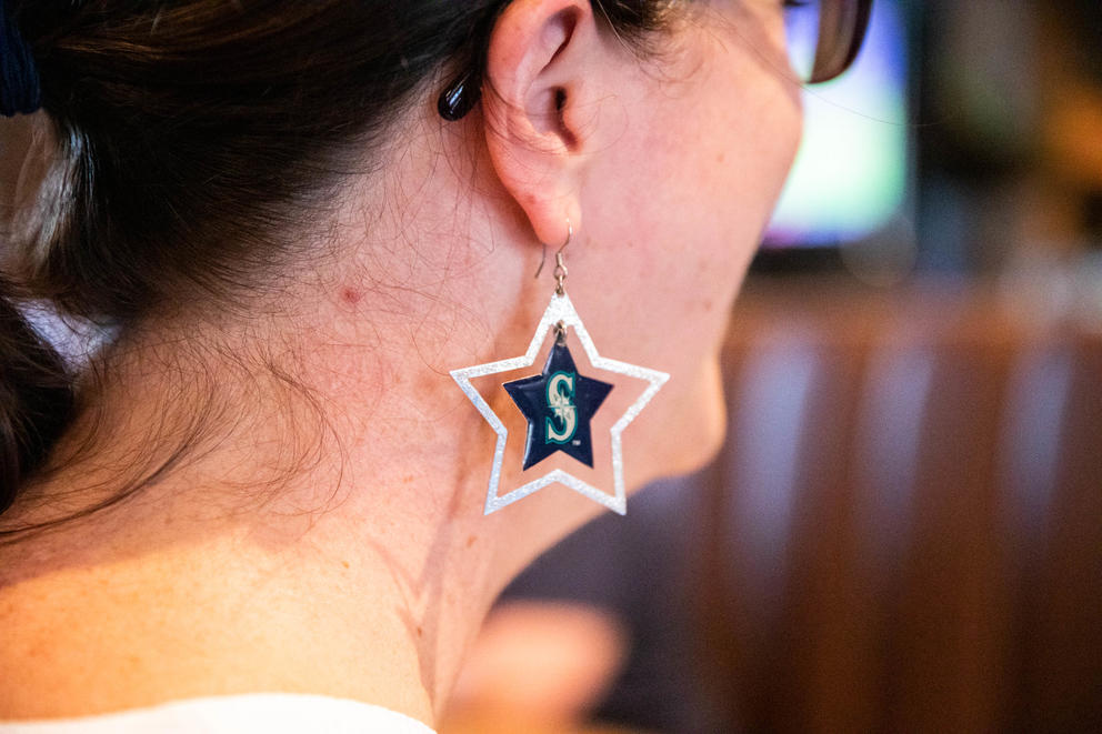 A close up of a woman's earring with the Mariners logo on it