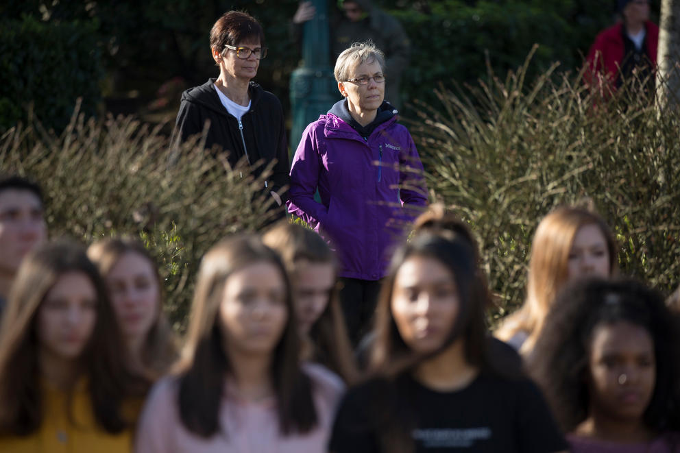 Neighbors Sharon Buren, left, and Cheryl Buren, right join on the sidewalk in front of the school as students link arms for 17 minutes, honoring the 17 killed at a school shooting in Parkland, Florida
