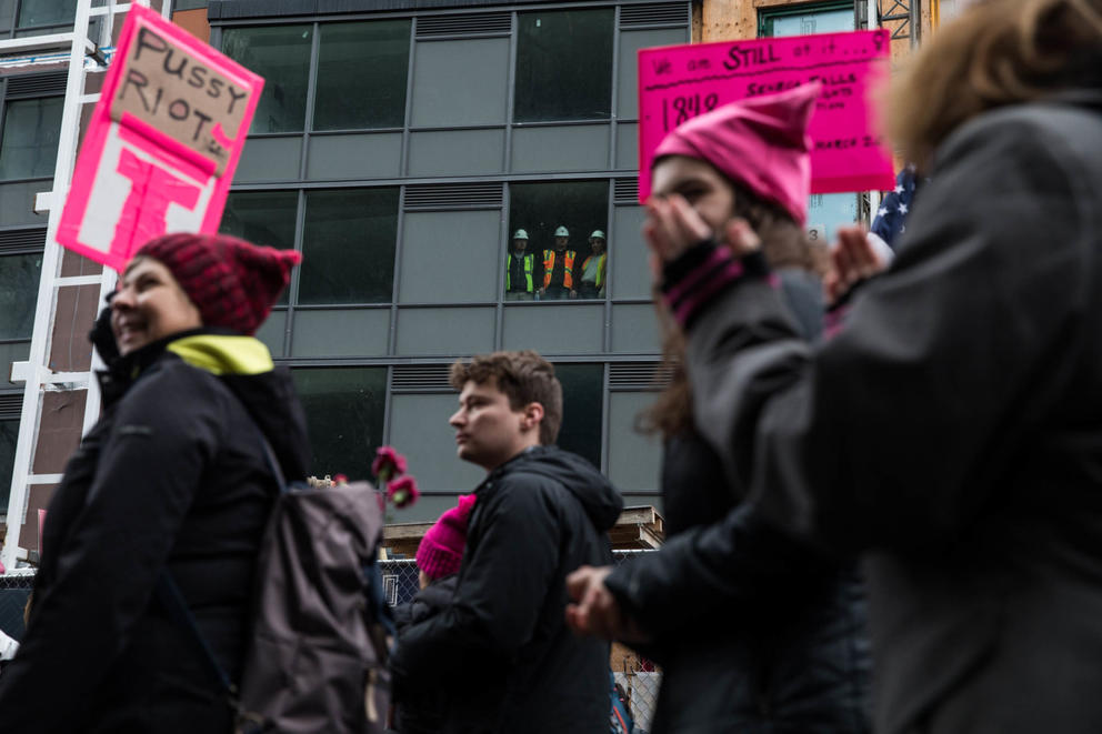 Construction workers in a nearby building gather in the window to watch the Seattle Women’s March 2.0 as it proceeds towards Seattle Center in Seattle, Jan. 20, 2018.