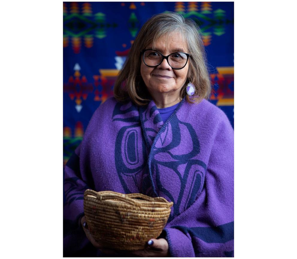 Woman in a purple garment and holding a basket smiles into the camera