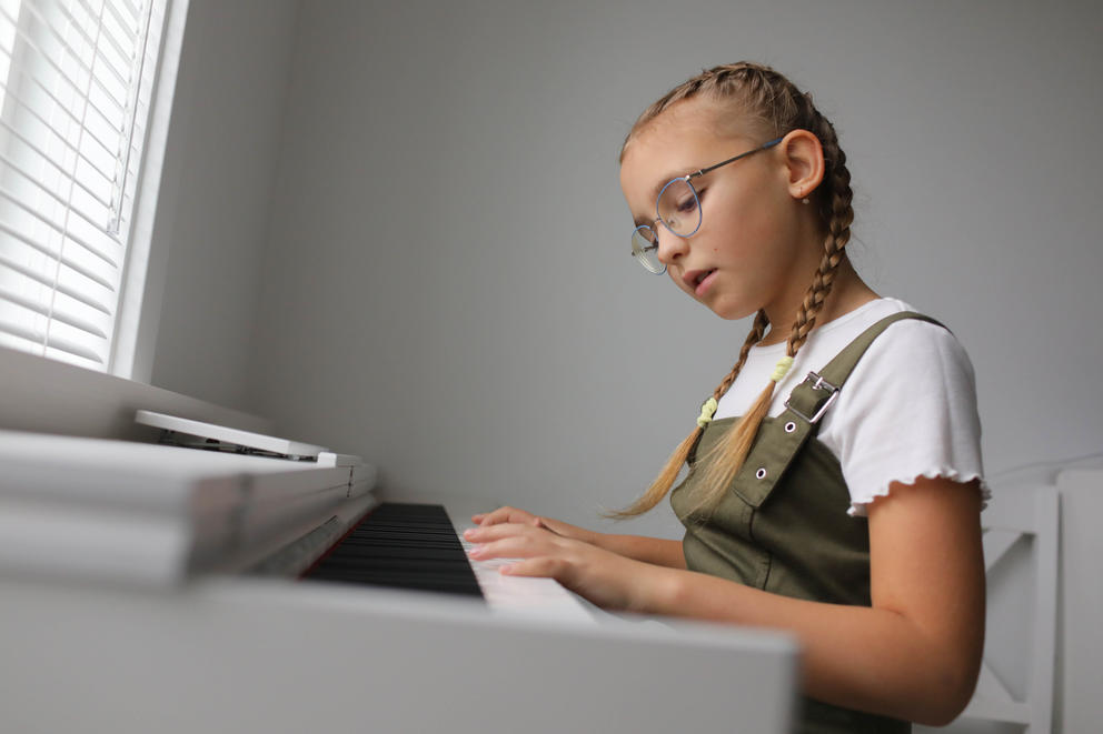 a young girl with braids and glasses plays piano
