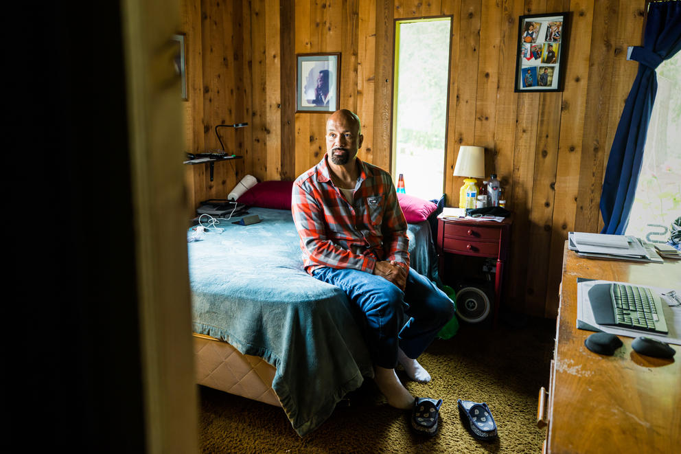 Nathaniel Sanders sits on a bed in a wood paneled room