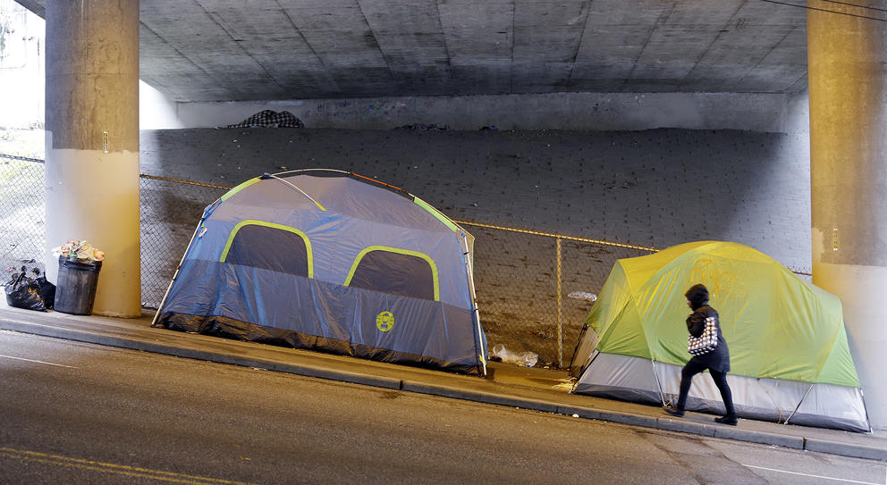 Tents are shown on a sidewalk under an overpass 
