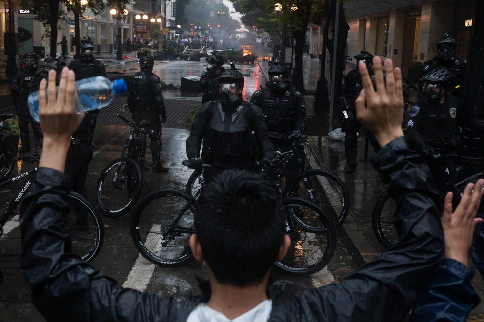 Protesters stand with raised hands in front of police officers