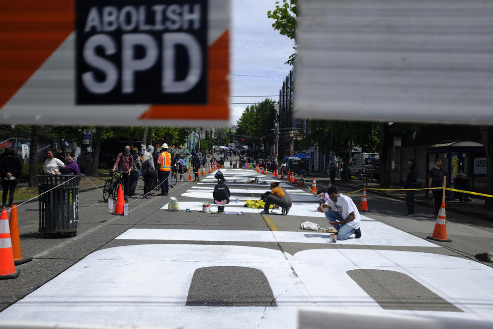 people kneeling on the ground painting a black lives matter mural on the street in seattle