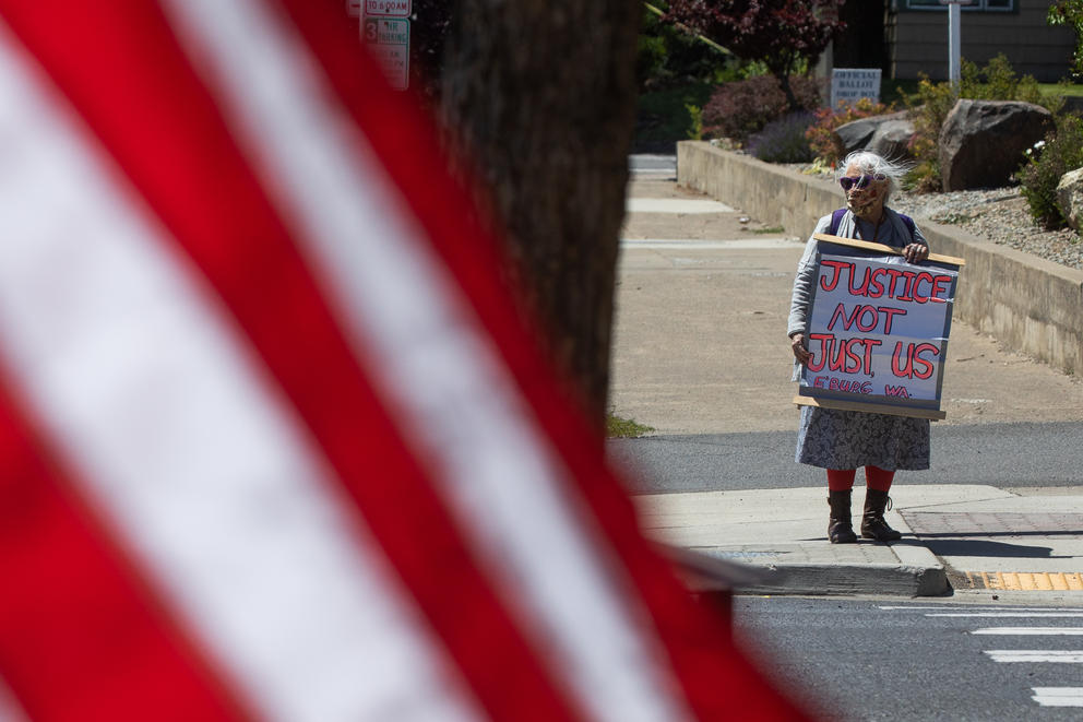 A woman stands with a sign with an American flag in the foreground