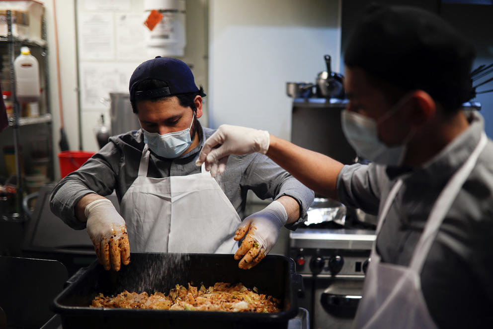 Kitchen workers wear surgical masks and gloves as they prepare food