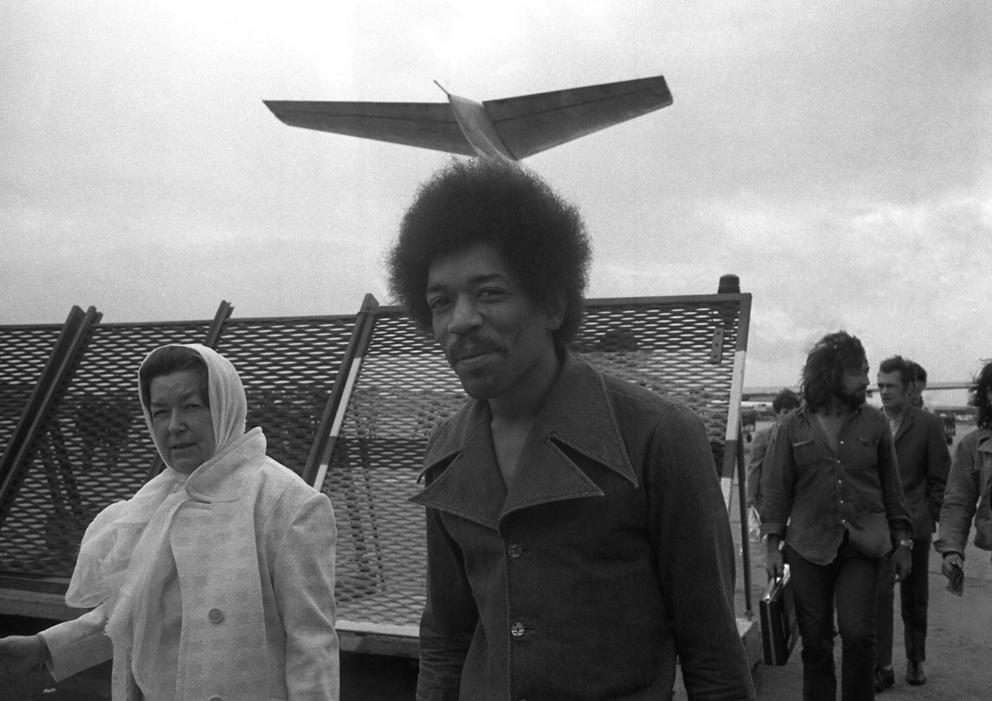 black and white photo of Jimi Hendrix in front of plane