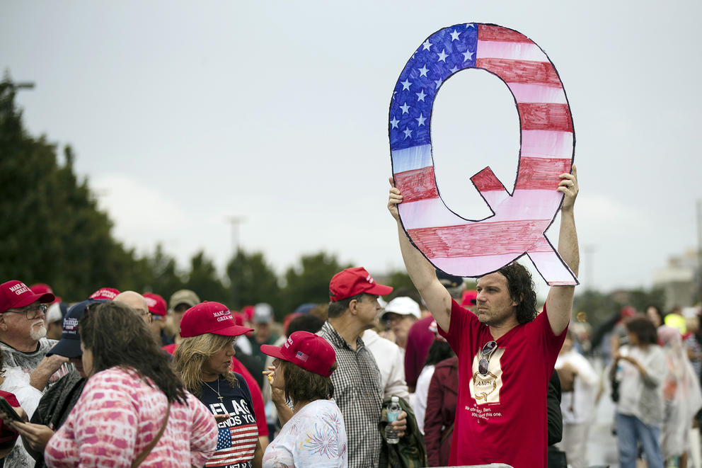 A person holds a 'Q' sign in a crowd