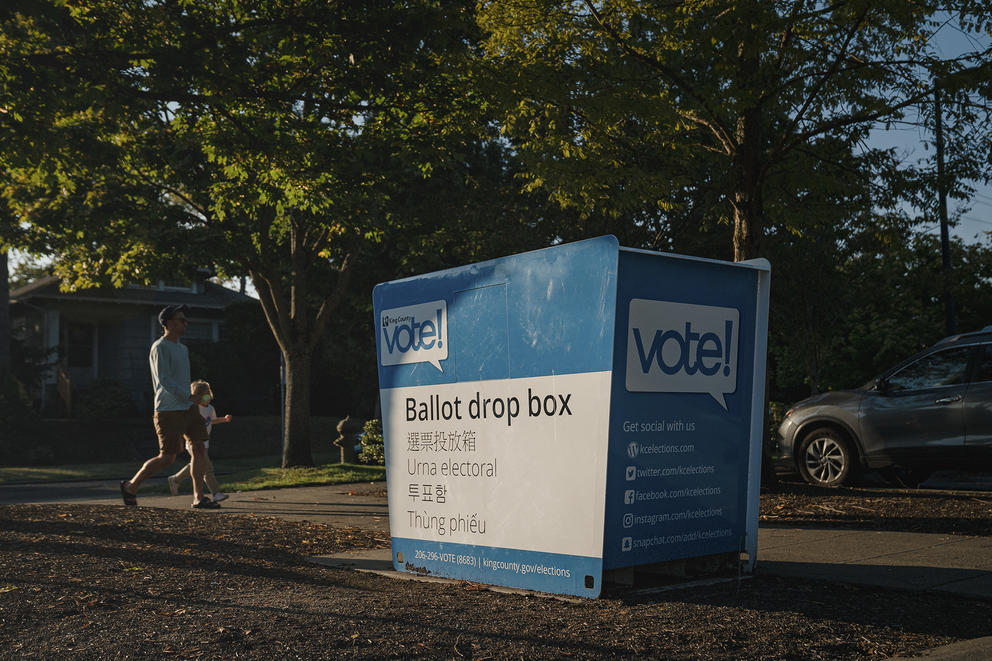 A father and his daughter walk by a ballot drop box