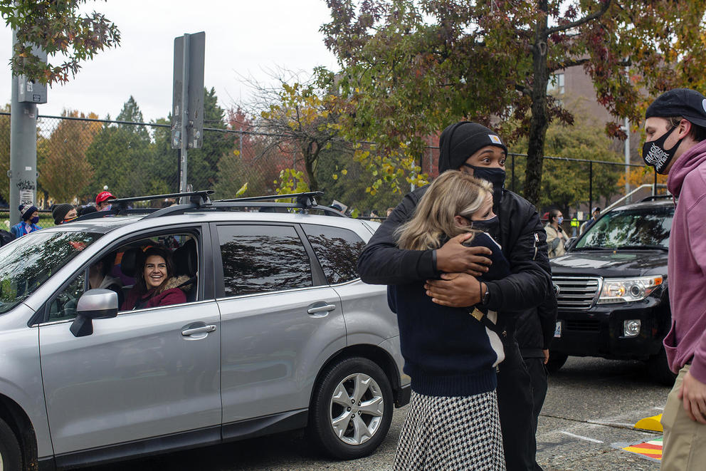 Smiling woman in a car next to people hugging in the street.