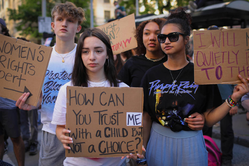 four young people hold signs at a protest