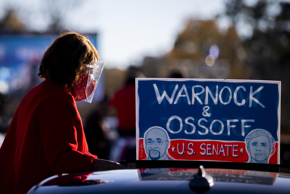 A woman stands on top of a car with a Warnock and Ossoff sign in background