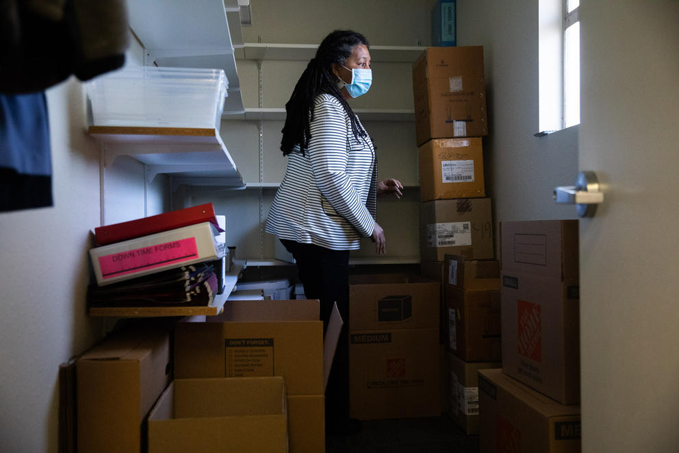 Sharon Dudash stands amid boxes in empty room, facing window