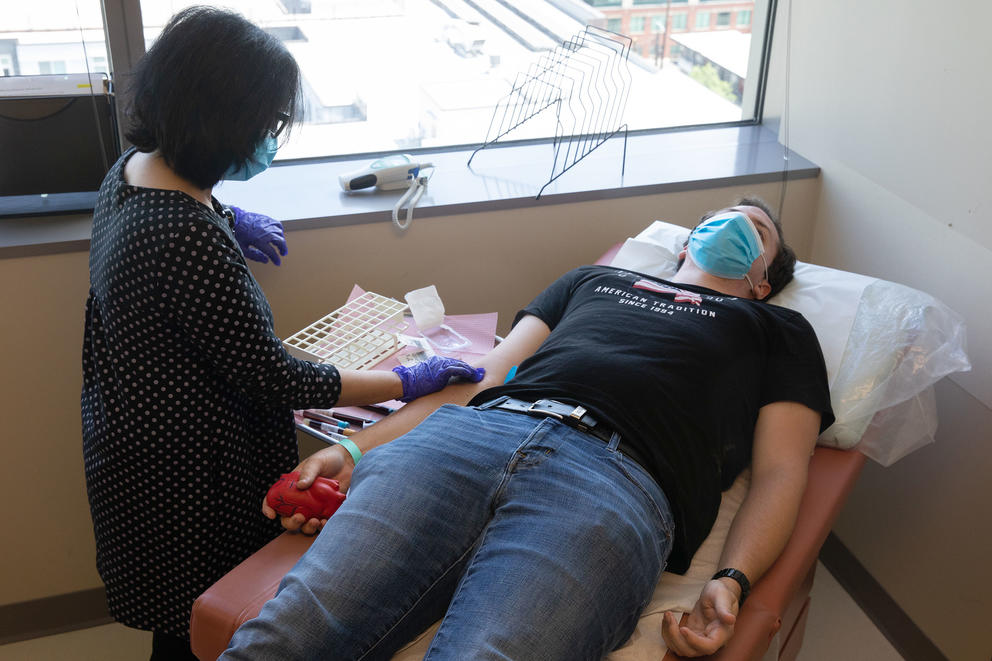Man in jeans and a t-shirt lying on exam table while getting blood drawn