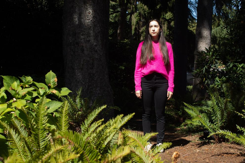 Margo Spindola stands outdoors under a tree with ferns in the foreground 