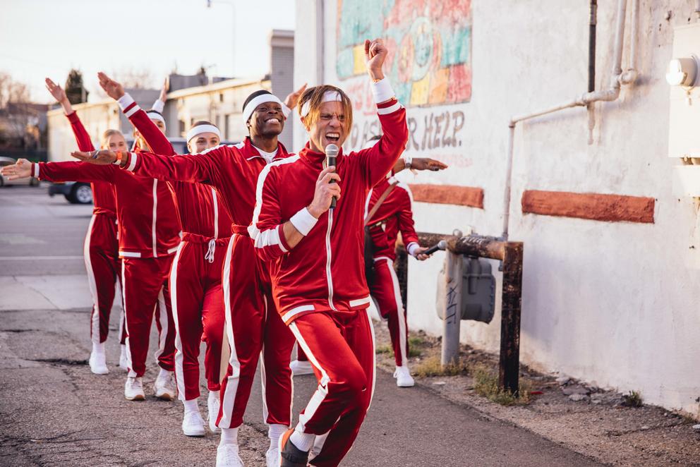 six people in a line, all wearing red tracksuits and dancing