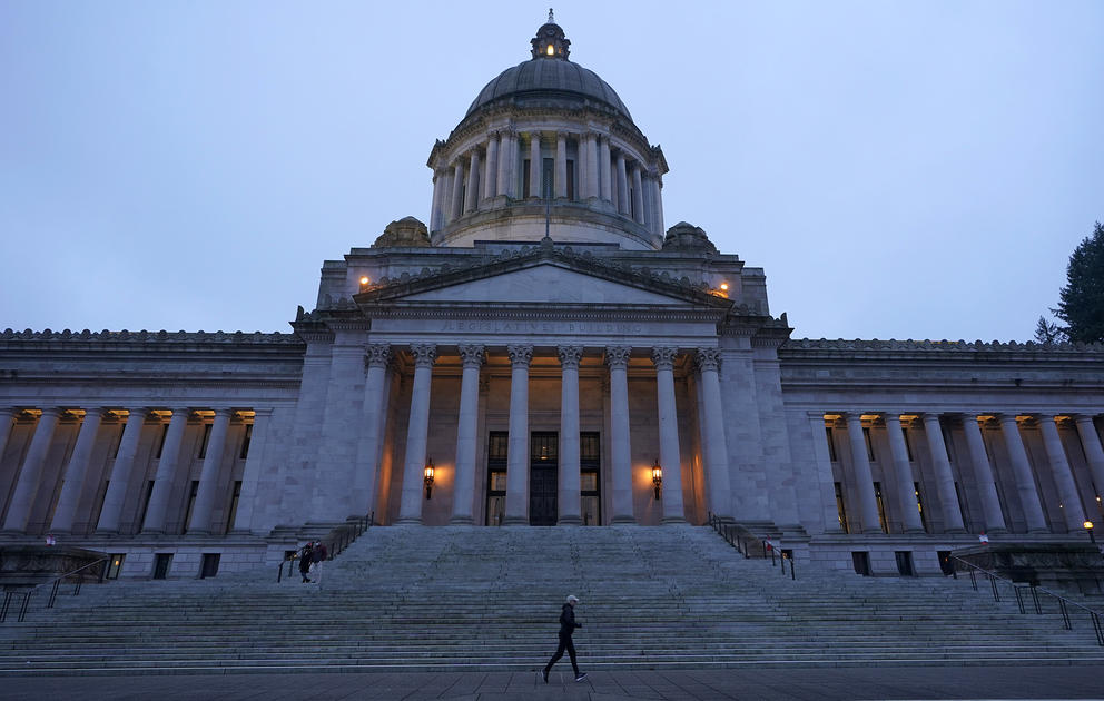 The Washington State Legislative Building and its dome are silhouetted as the light dims and a jogger passes by the building's stone steps
