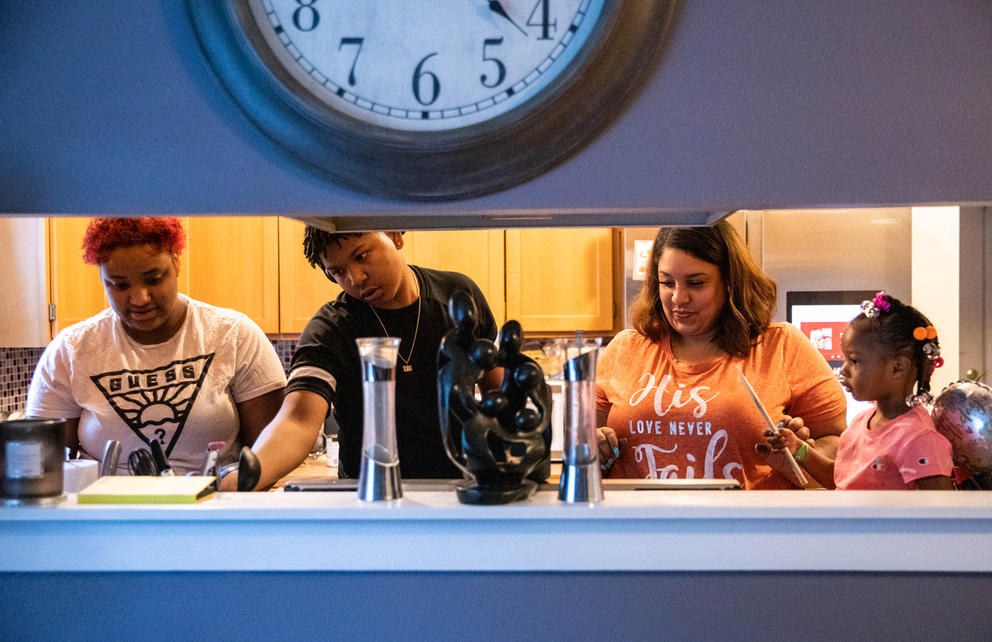 two women, a young man, and a toddler cook together in a kitchen