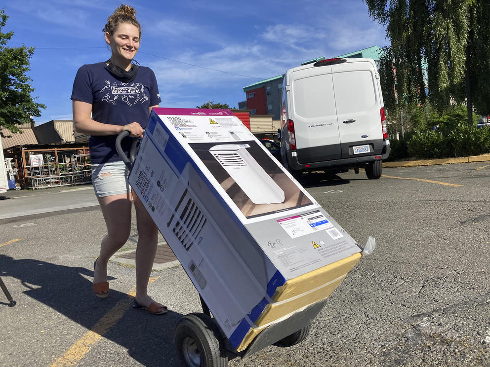 a smiling person wheels a cart holding an air conditioning unit