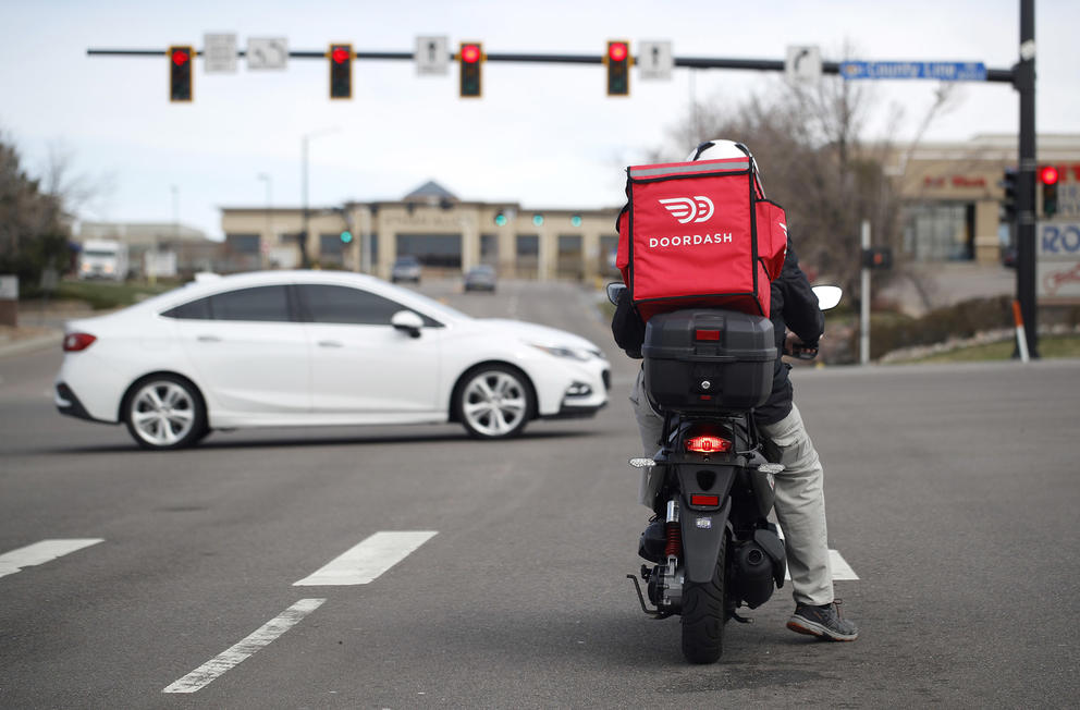 a door dash delivery person sits on a scooter at a red light