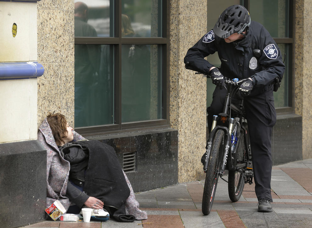 Seattle police officer on a bike speaks to women sitting on the sidewalk