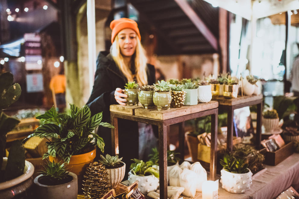 Woman with long blonde hair and orange hat arranges planters and potts on shelving