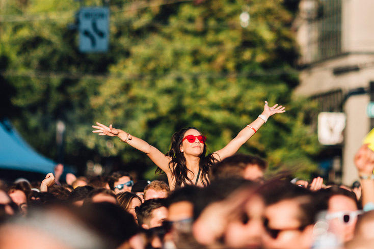 Person in a crowd opens up their arms into the sky, trees and blue sky in the background