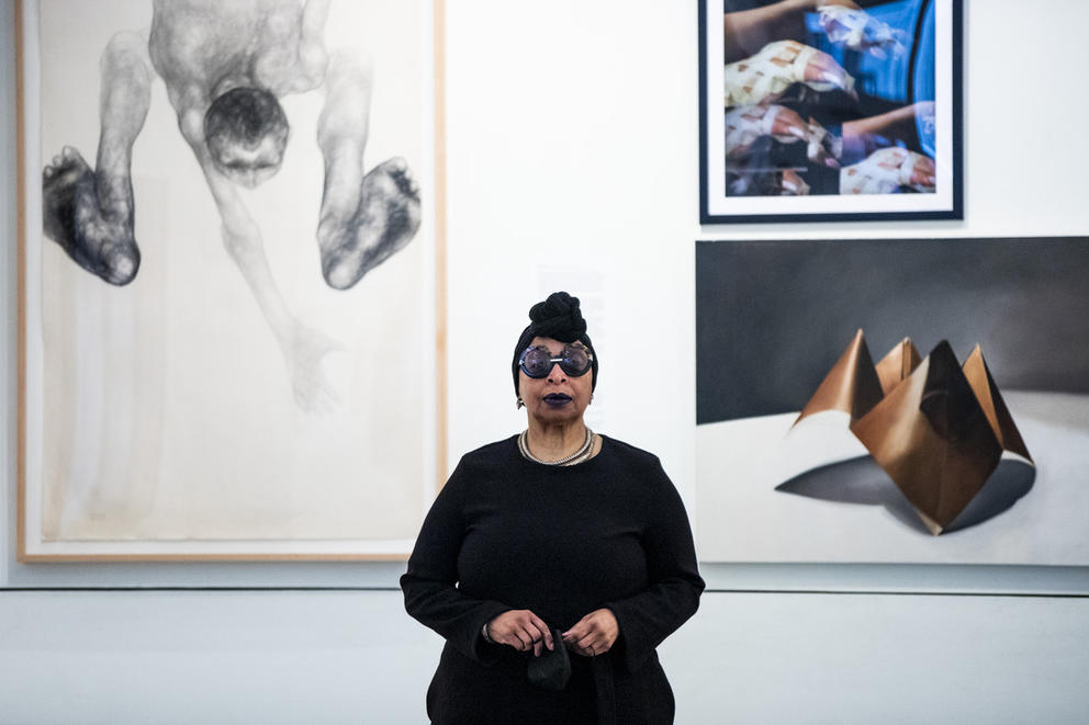Person dressed in black with headscarf and sunglasses in front of art