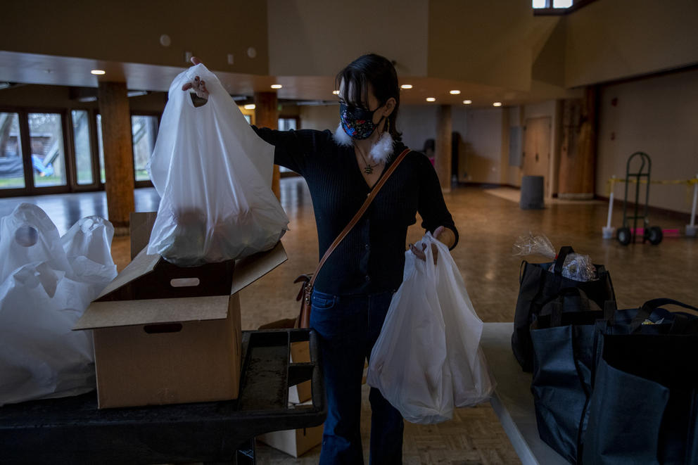A woman wearing a face mask and feathered earrings picks up plastic grocery bags