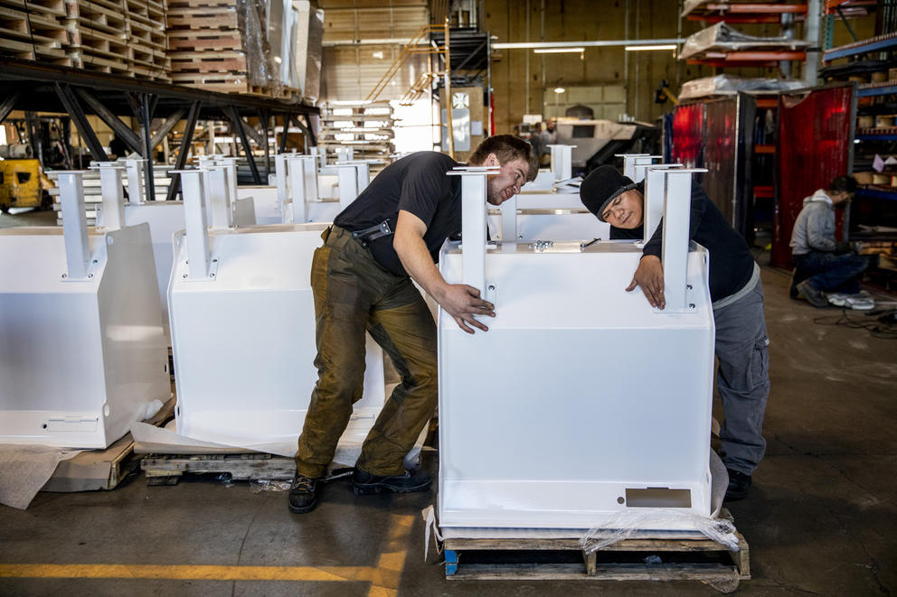 Two workers put together white steel pieces that form a ballot dropbox.
