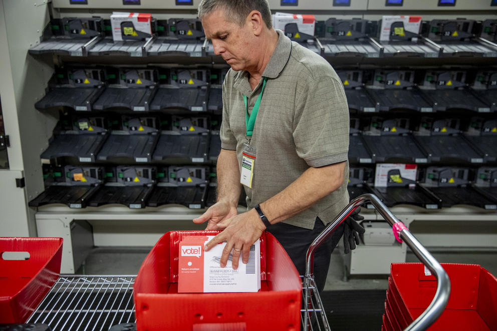 An election worker handles ballots in a red sorting tray.