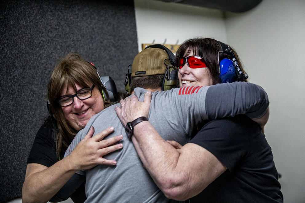 Jan, 62, left, and Melissa Elmer, 68, hug John Abbitt after he taught them how to shoot a gun for the first time at West Coast Armory in Bellevue during a Pink Pistols range meetup on May 18, 2019. The couple recently purchased their first firearm and came to Pink Pistols to learn how to shoot it. “I’m comfortable with this group of people more than any other group,” Jan says. (Photo by Dorothy Edwards/Crosscut)