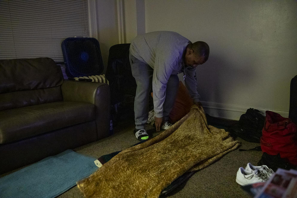 A man makes a space to sleep on the floor of his uncle's apartment