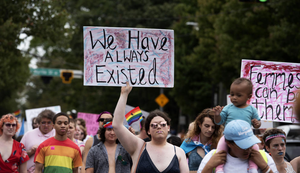 A person in a crowd holds a sign that reads "We have always existed."