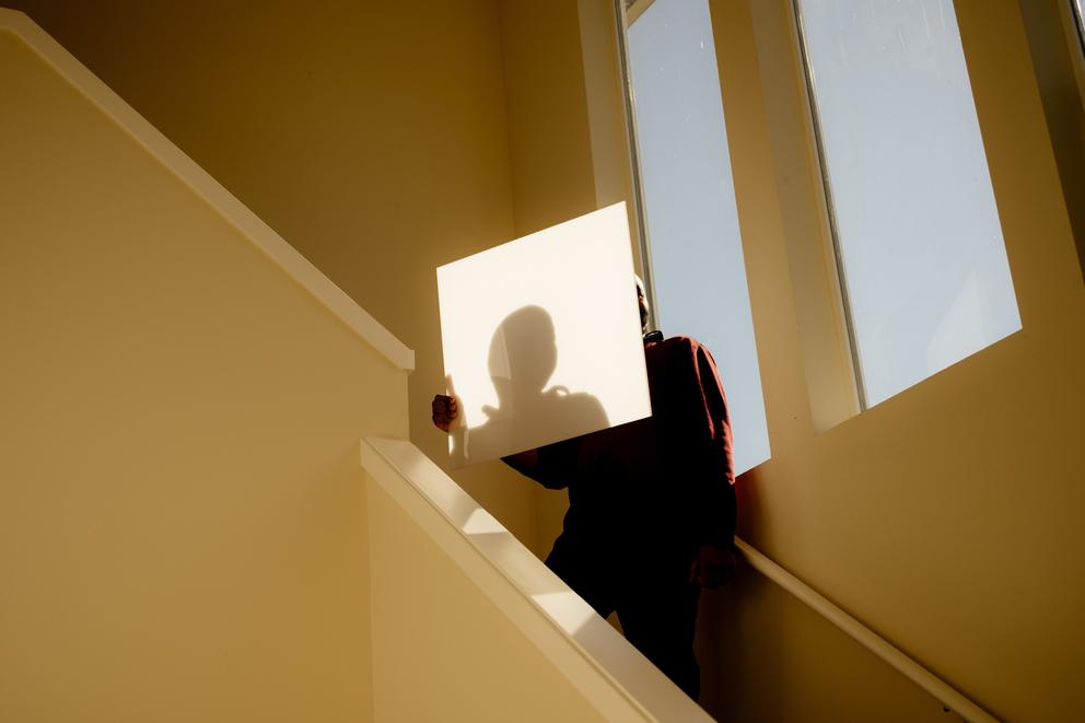 A man stands on a staircase, his face blocked, a window behind him 