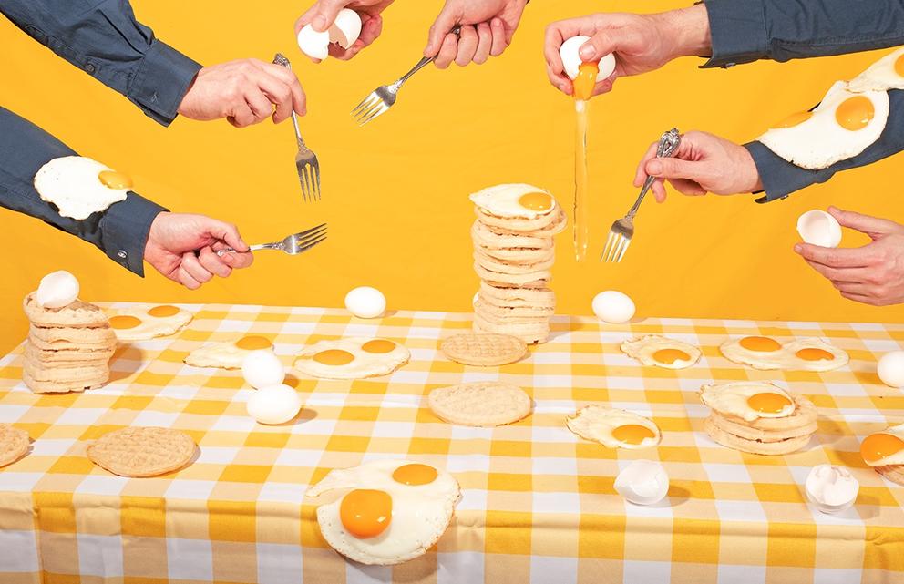 Photo with yellow background and yellow-and-white gingham table cloth featuring all sorts of omelets and hands eating with forks