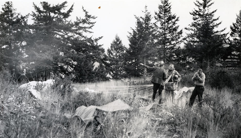 Men with parachutes stand in a clearing
