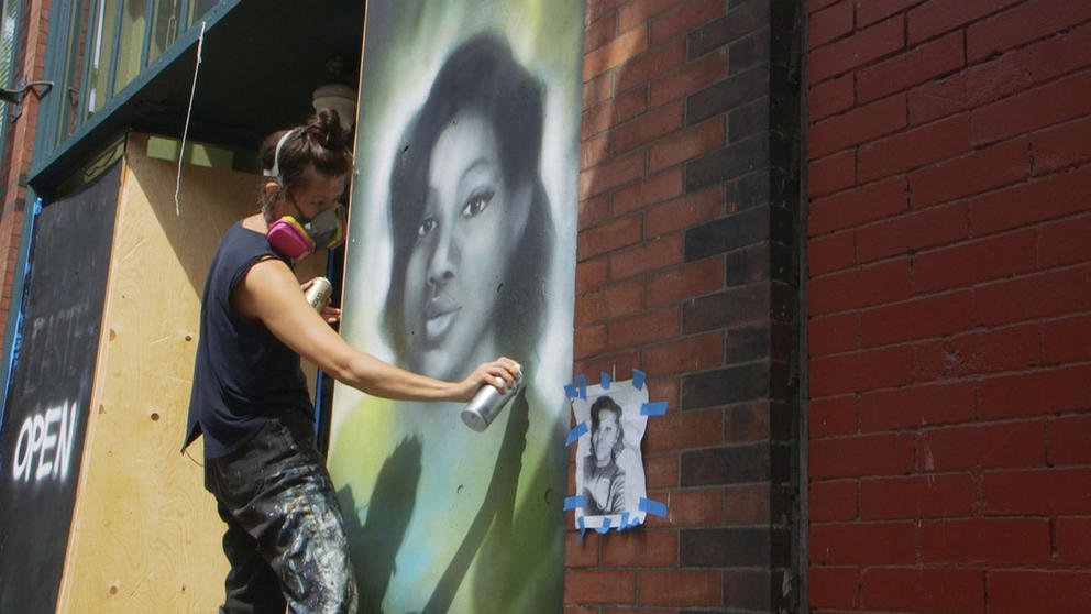 A woman works on a mural using spray paint