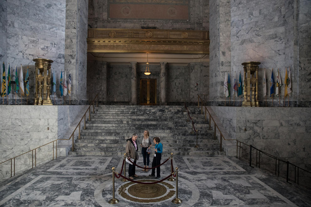 Visitors stand in the rotunda of the state Capitol in Olympia, by a bronze seal of George Washington and surrounded by the Capitol's marble halls.