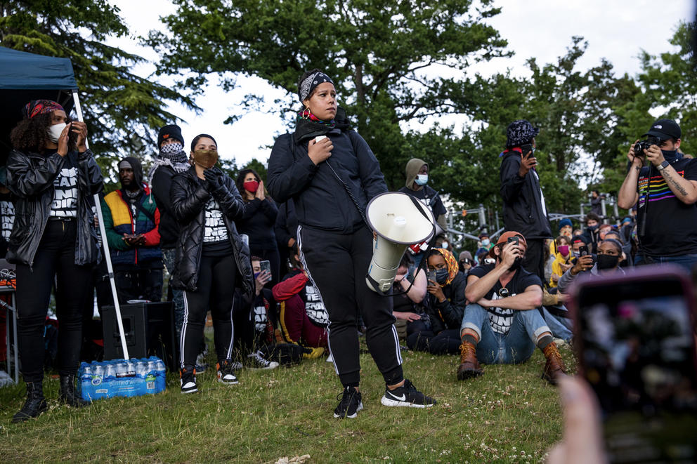 Nikkita Oliver holds a megaphone while standing in the center of a group of people